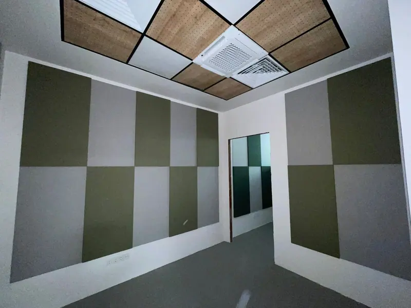 Yeşil ve gri kumaş kaplı panellerle düzenlenmiş duvar ve delikli ahşap tavan